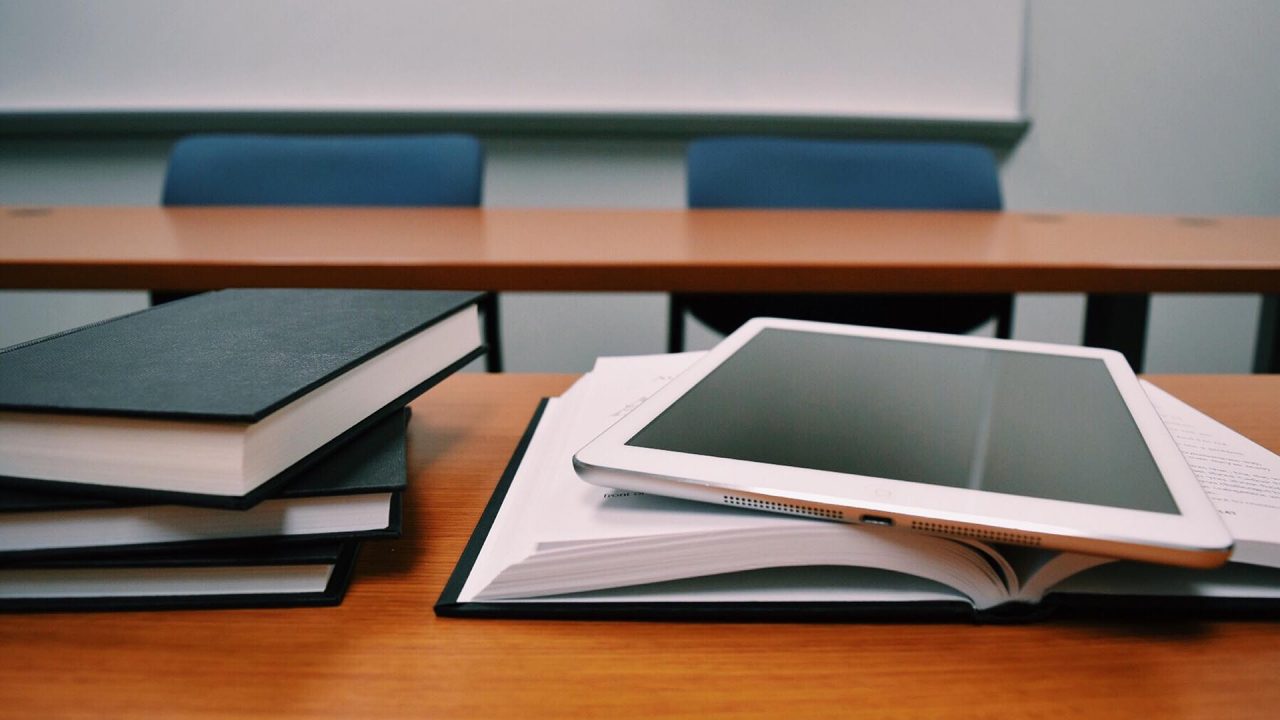 Una pila de tres libros cerrados a la izquierda y un libro abierto donde apoya una tablet